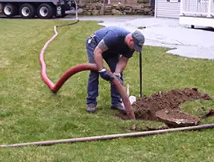 Septic pumping technician servicing a residential septic tank with a vacuum hose in Providence, RI