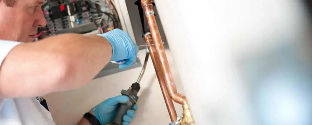Water heater repair technician testing copper pipe connections and controls in Providence, RI